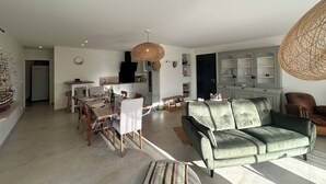 Un salón amplio con un sofá verde, un comedor con sillas de madera y una cocina con armarios blancos.
