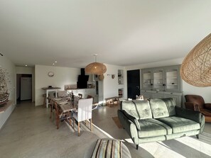 A spacious living room with a green sofa, a dining area with wooden chairs, and a kitchen with white cabinets. - Villa "La marine" with garden, terrace and swimming pool (Les mathes)