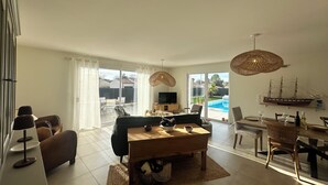 Amplia sala de estar con sofá, mesa de centro y comedor. Hay un televisor, un modelo de barco y vistas a una piscina y un patio trasero.