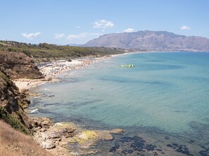 Eine Küstenlandschaft mit Strand, felsigen Klippen und Bergen im Hintergrund.
