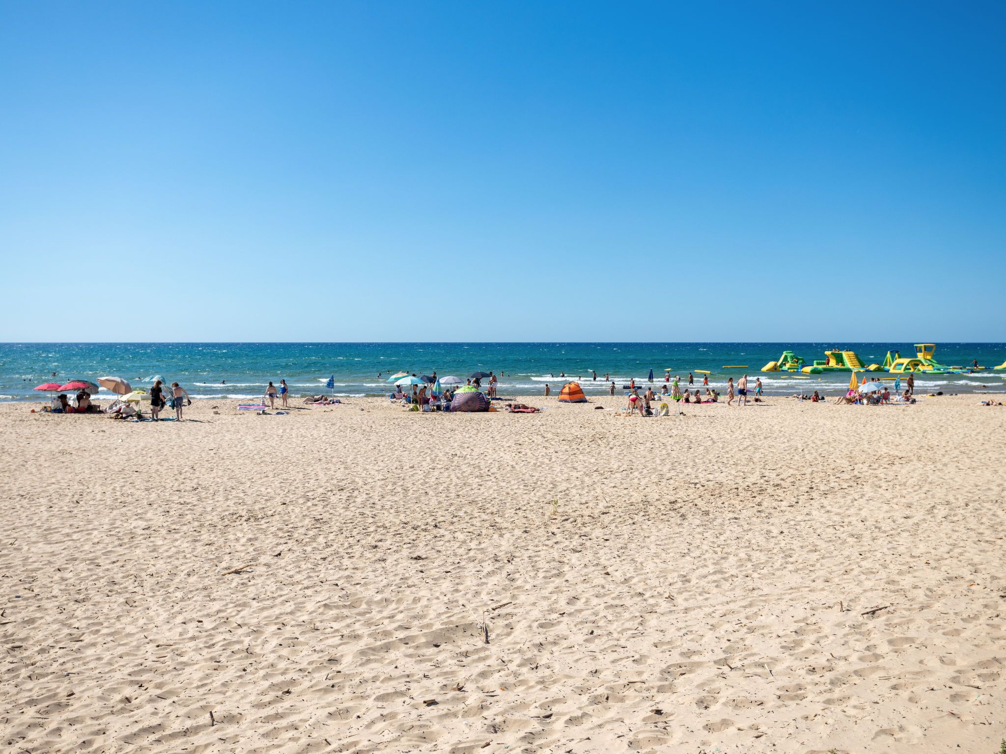 Ein weiter Sandstrand mit Menschen und bunten Strandstühlen.