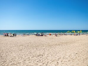 Ein weiter Sandstrand mit Menschen und bunten Strandstühlen.