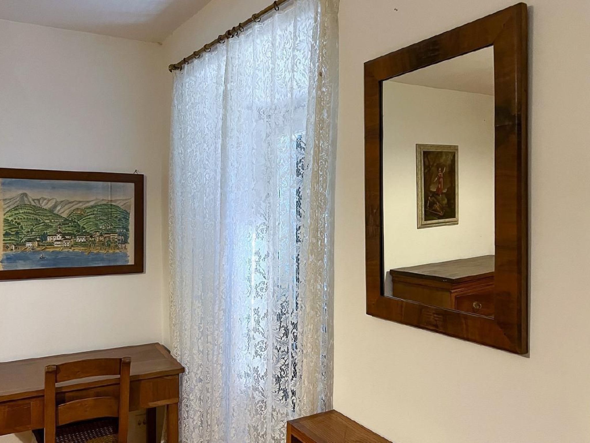 Habitació amb escriptori de fusta, un mirall gran i un quadre a la paret.