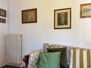 Ein Zimmer mit einem Heizkörper, einem blumengemusterten Sofa mit Kissen und gerahmten Bildern an der Wand.