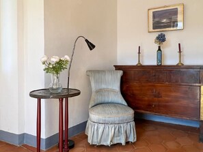 Eine Sitzecke mit rundem Tisch, einem Sessel, einer Stehlampe, einem Schminktisch und einem gerahmten Bild an der Wand.