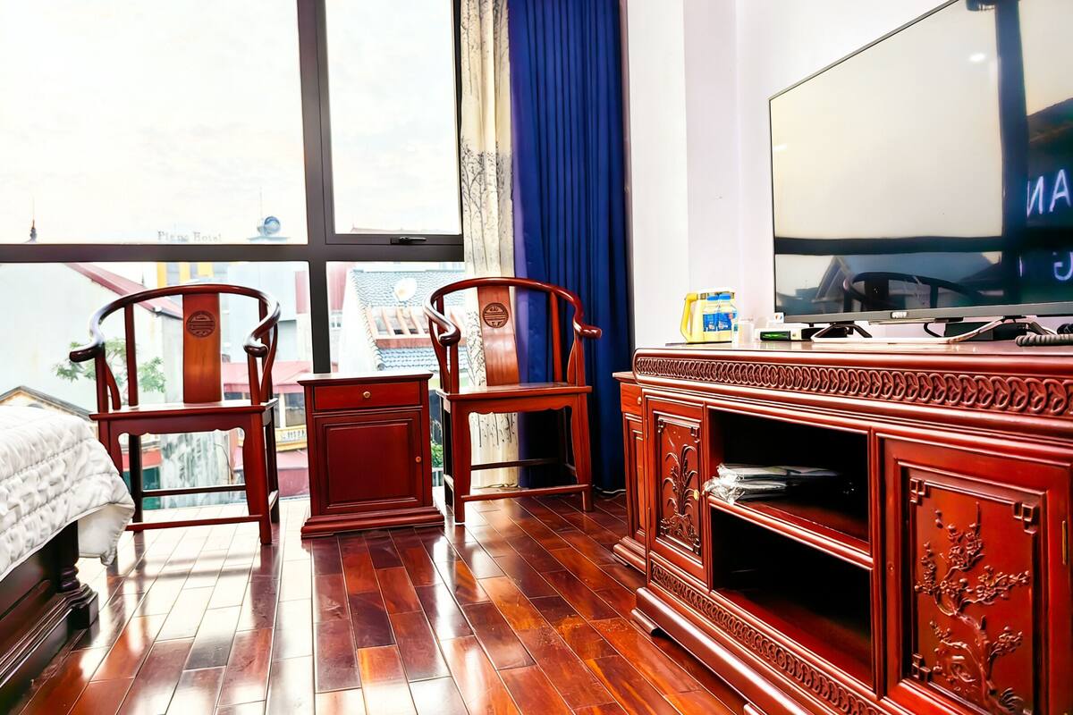 A hotel room with a large window, wooden furniture, and a flat-screen TV.