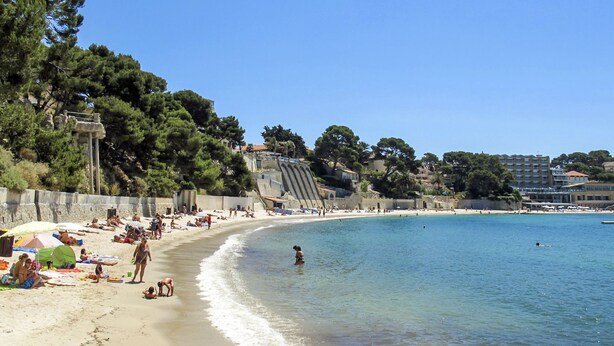 Una spiaggia con persone che prendono il sole e nuotano, un cielo azzurro limpido e edifici sullo sfondo.