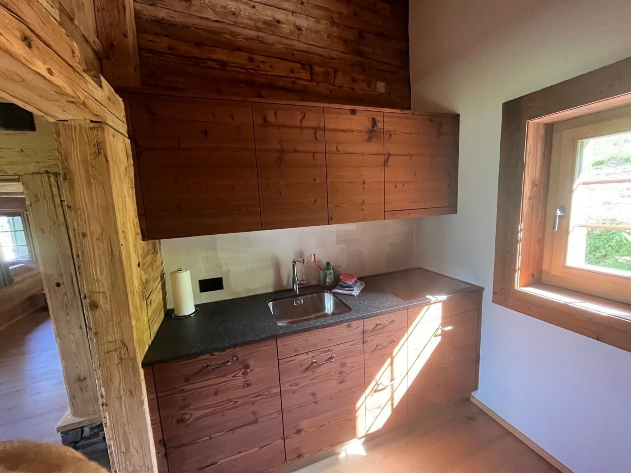 Une cuisine avec des meubles de rangement en bois, un plan de travail noir et une fenêtre.