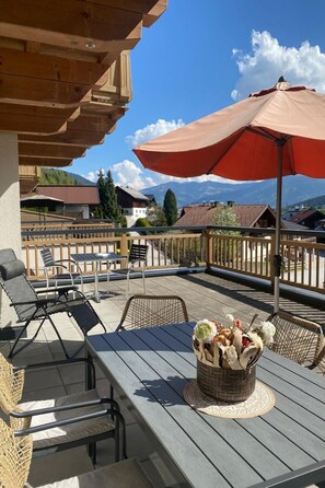 Eine Terrasse im Freien mit Holzmöbeln, einem großen Sonnenschirm und einem Korbwesen mit Blumen.