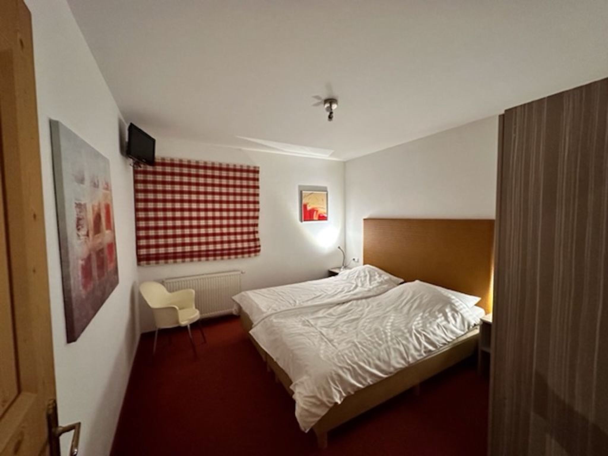 A hotel room with a single bed, a chair, a radiator, and a ceiling fan.