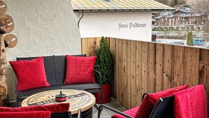 An outdoor patio with a round table, two chairs, and a sofa with red cushions. A wooden fence and a banner reading "Haus Pudleiner" are visible. - Grandview Collection Luxus-Wohnung in Kaprun by Interhome (Kaprun)