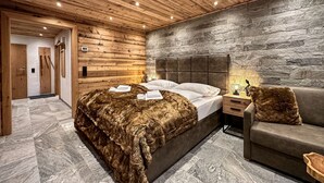 A modern bedroom with a wooden ceiling, stone wall, and a bed with a fur throw. - Grandview Collection Luxus-Wohnung in Kaprun by Interhome (Kaprun)