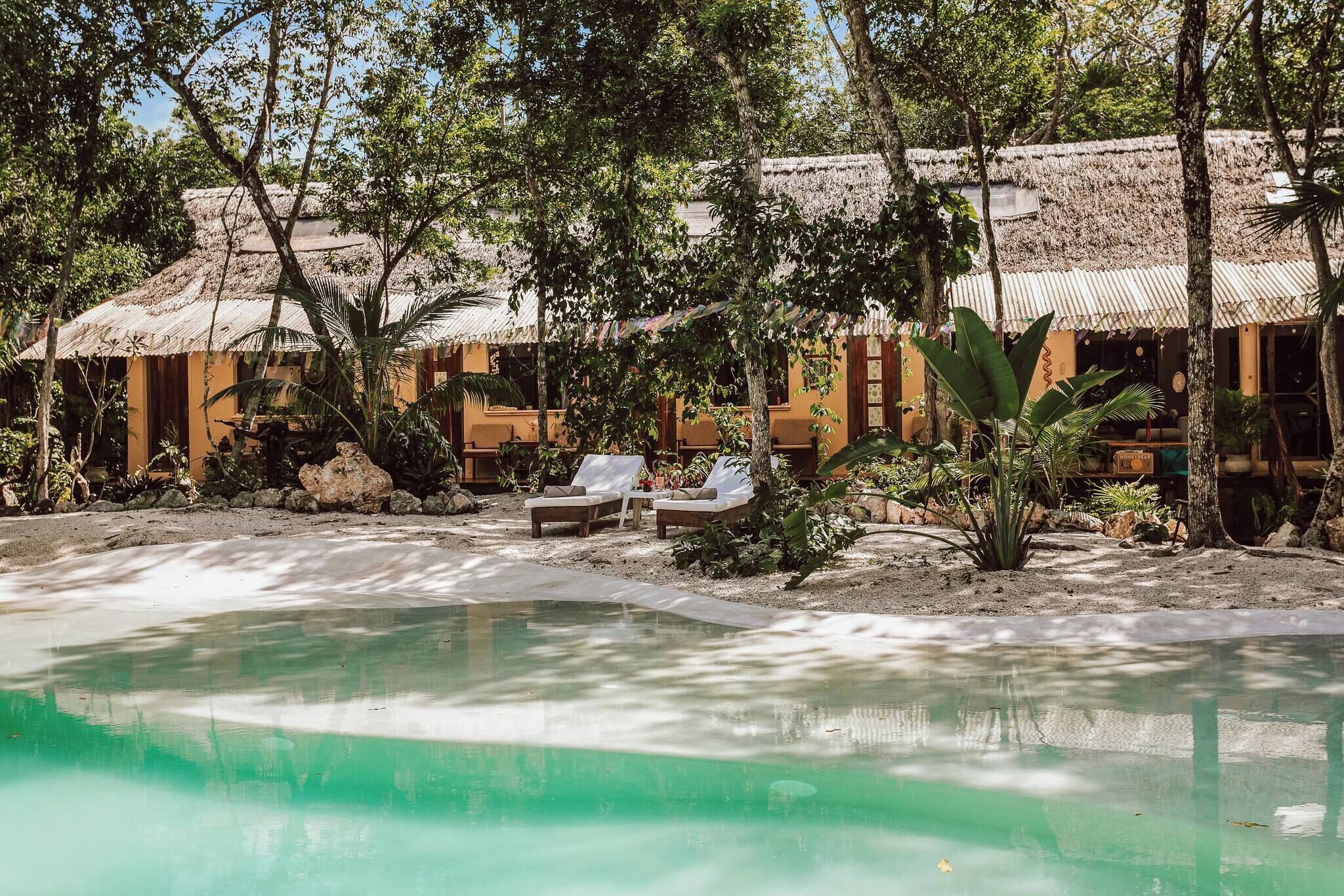 A pool area with lounge chairs and a thatched-roof building.