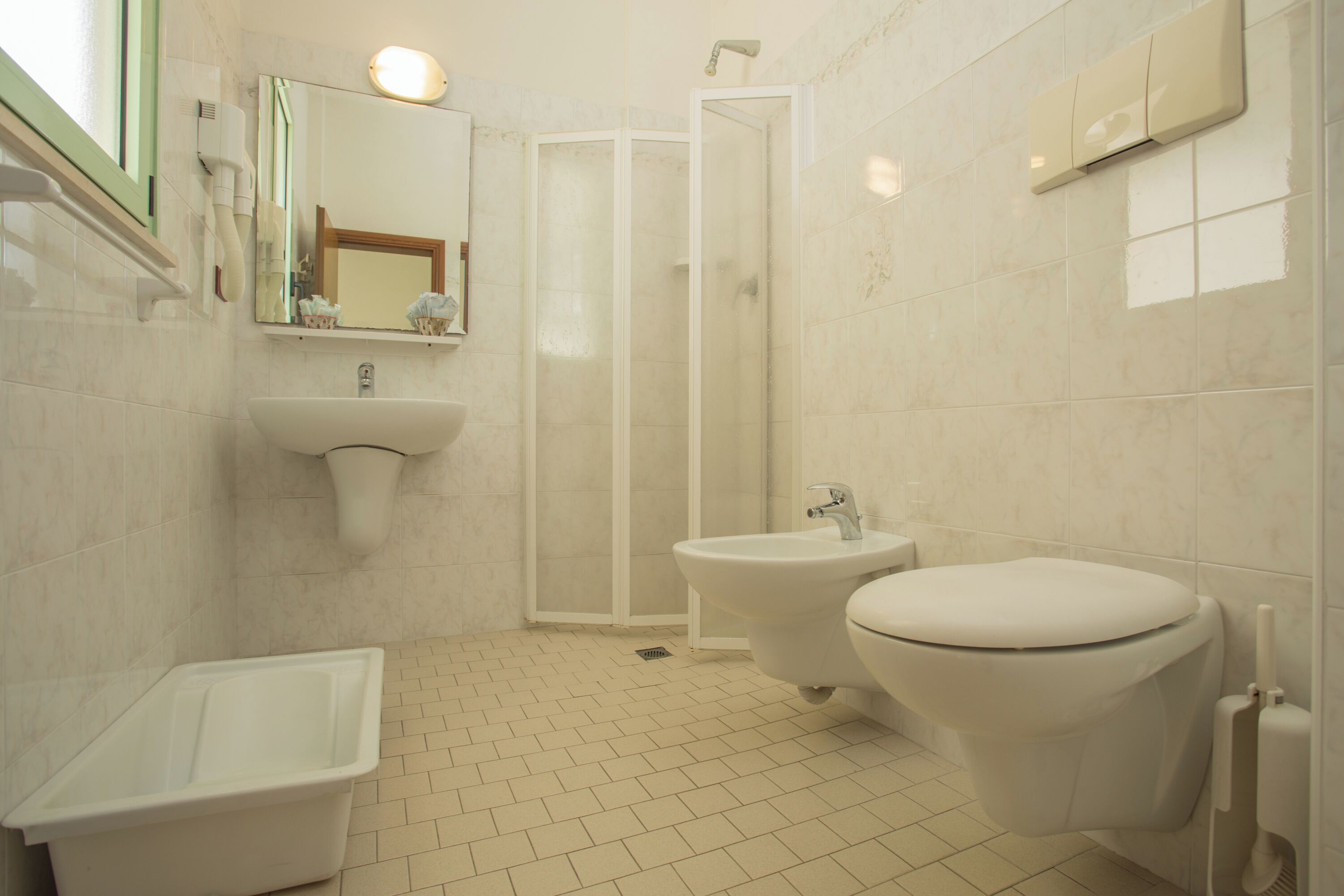 A bathroom with a sink, bidet, toilet, and a shower enclosure.