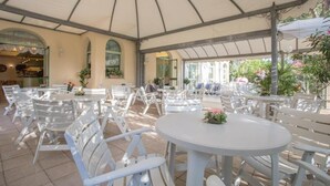 An outdoor patio with white tables and chairs, a covered area with a curved roof, and potted plants. - Hotel Dover Rooms & Coffee - Adults Friendly (Cervia)