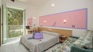 A bedroom with a bed, a desk, a chair, a green sofa, and a balcony with a view of trees. - Hotel Dover Rooms & Coffee - Adults Friendly (Cervia)