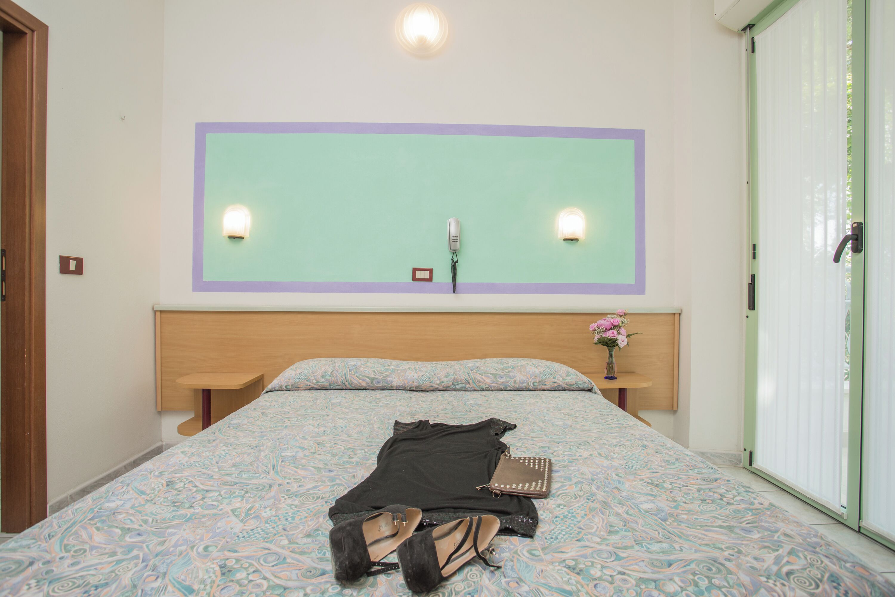 A neatly made bed with a patterned bedspread, a bedside table with a lamp, and a wall-mounted light fixture.