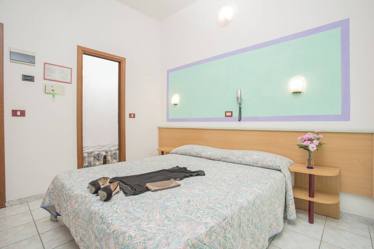 A bedroom with a bed, a nightstand, a mirror, and a wall-mounted telephone.