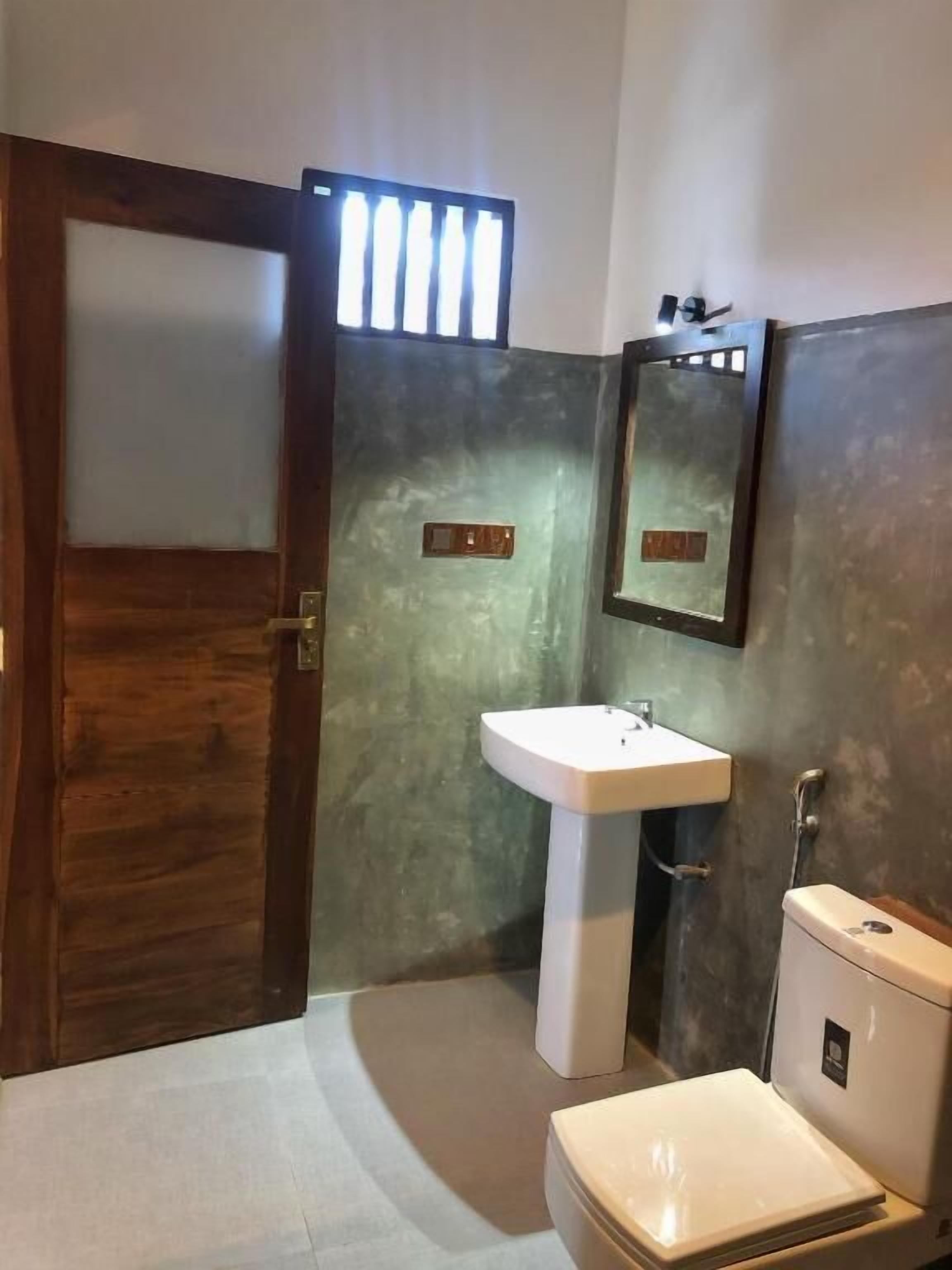 A bathroom with a wooden door, a white sink, a mirror, and a toilet.