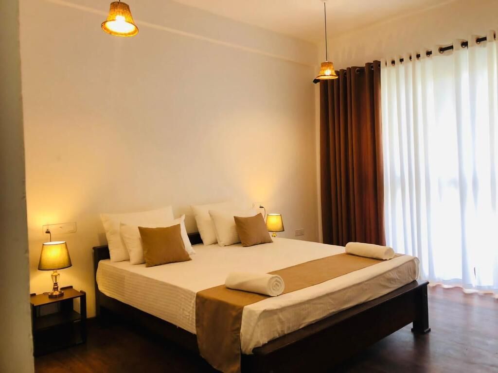 A hotel room with a large bed, two bedside lamps, a window with curtains, and a wooden floor.