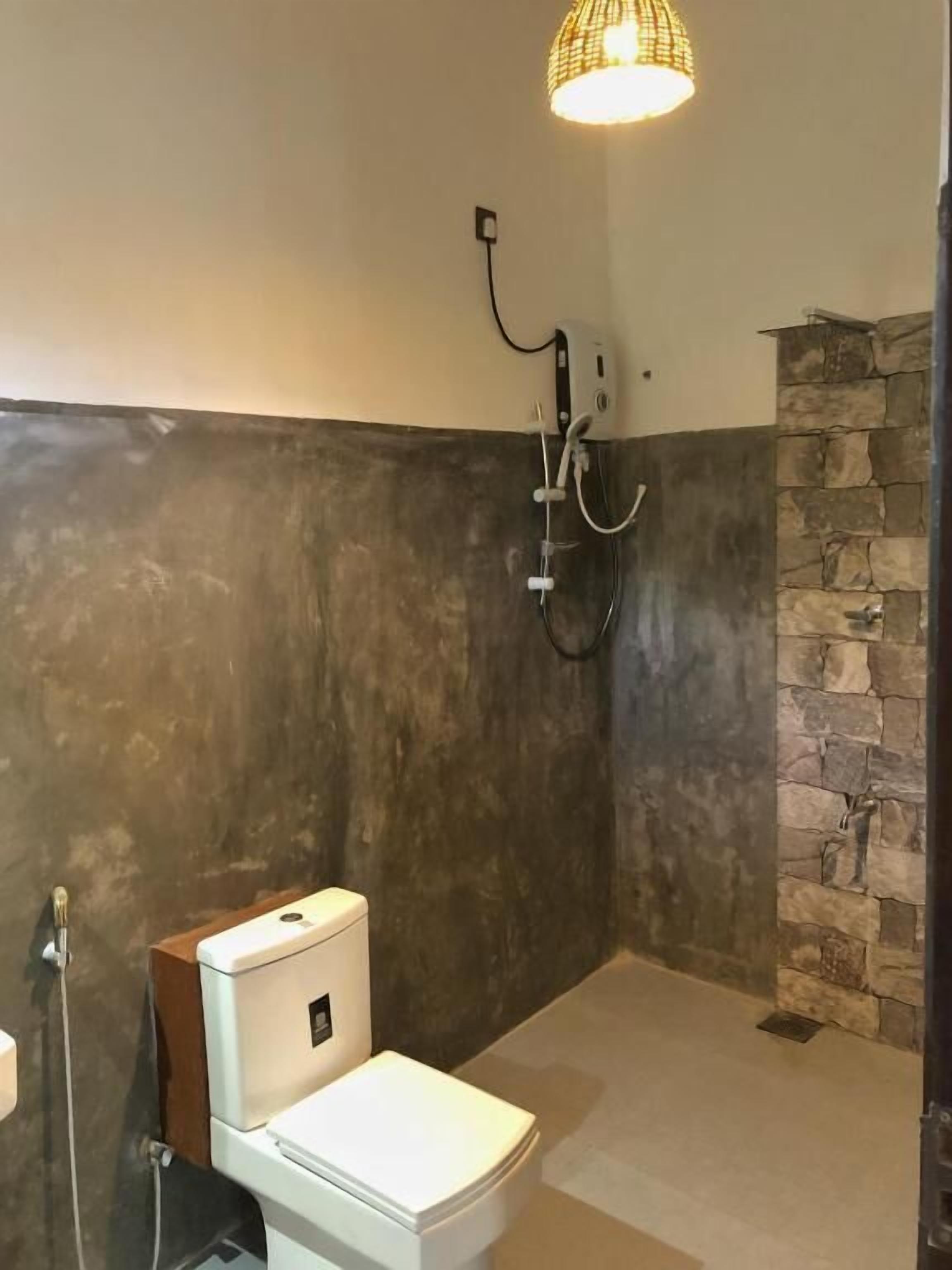 A modern bathroom with a stone accent wall, a white toilet, and a shower area.