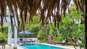 Un espace piscine doté de chaises longues et d’un coin salon abrité, le tout entouré d’une végétation luxuriante.