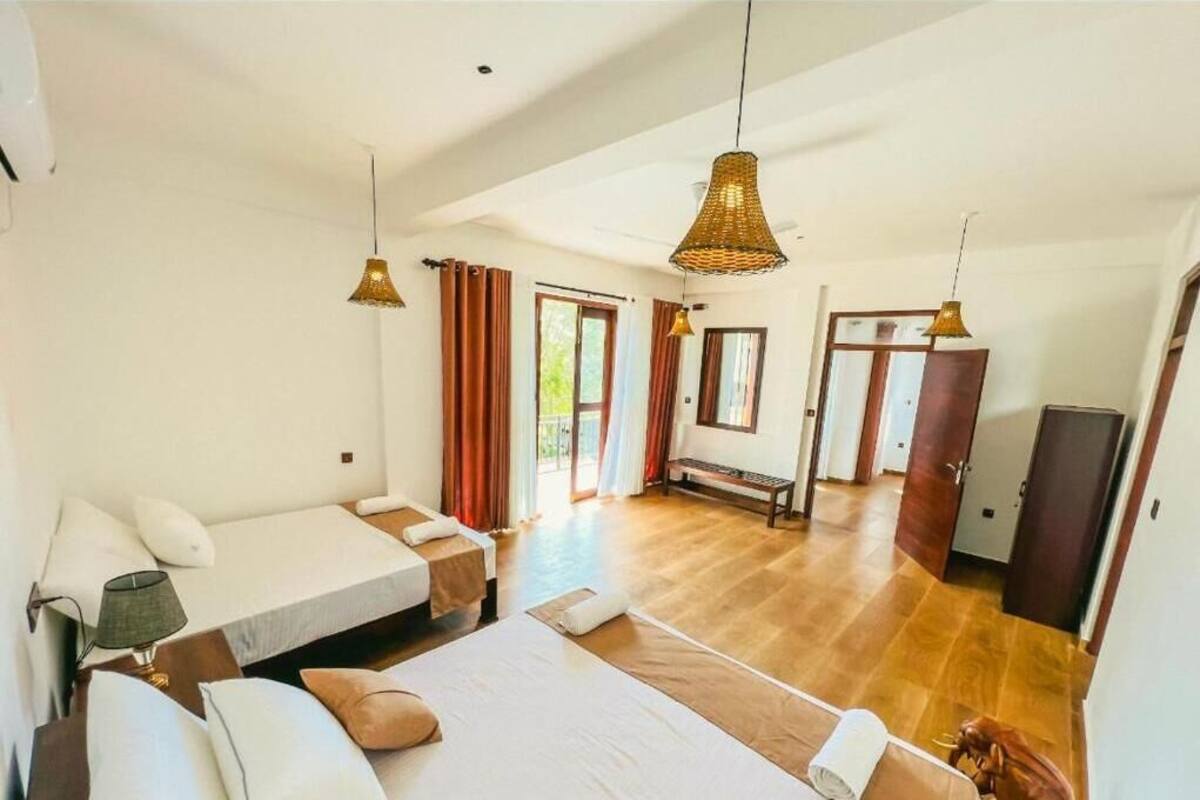 A spacious room with a large bed, a bench, and a wardrobe. There are curtains on the windows and a hanging light fixture.