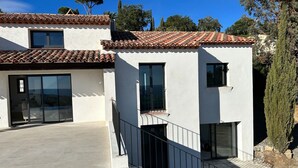 Ein modernes, zweistöckiges Haus mit Ziegeldach, großen Fenstern und einem Balkon.