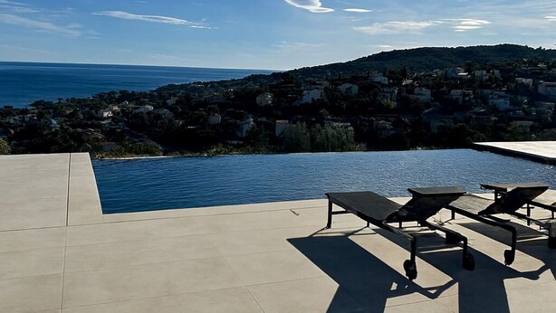 Ein Pool ohne Ende mit Liegestühlen, blauem Himmel und Blick auf eine Küstenstadt.