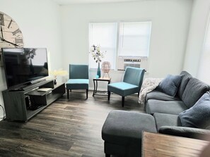 Una sala de estar con televisor, dos sillones, un sofá y una mesa de centro de madera.