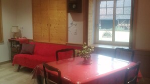 Ein Essbereich mit einem roten Tisch, Holzstühlen, einem Deckenventilator und Blick durch ein Fenster.