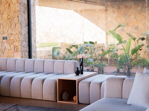 A modern living room with a beige sectional sofa, a wooden coffee table, and a stone wall. - Villa Eleven Marrakech (Marrakech)
