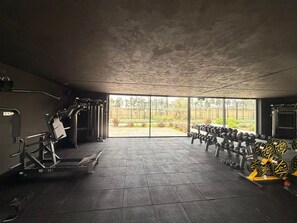 A gym with exercise equipment, a large window, and a view of a garden. - Villa Eleven Marrakech (Marrakech)