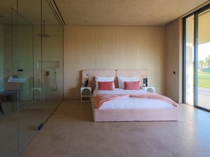 Ein modernes Schlafzimmer mit einem großen Bett, einer Duschkabine aus Glas und Blick ins Freie.
