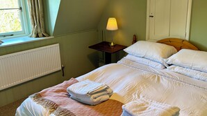 A bedroom with a bed, a nightstand, a lamp, a window with curtains, and a radiator. - Cosy one bedroom flat in a country house. (Bromham)