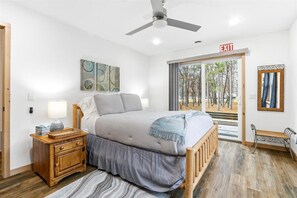 Ein Schlafzimmer mit Bett, Nachttisch, Lampe und Blick auf Bäume durch ein Fenster.