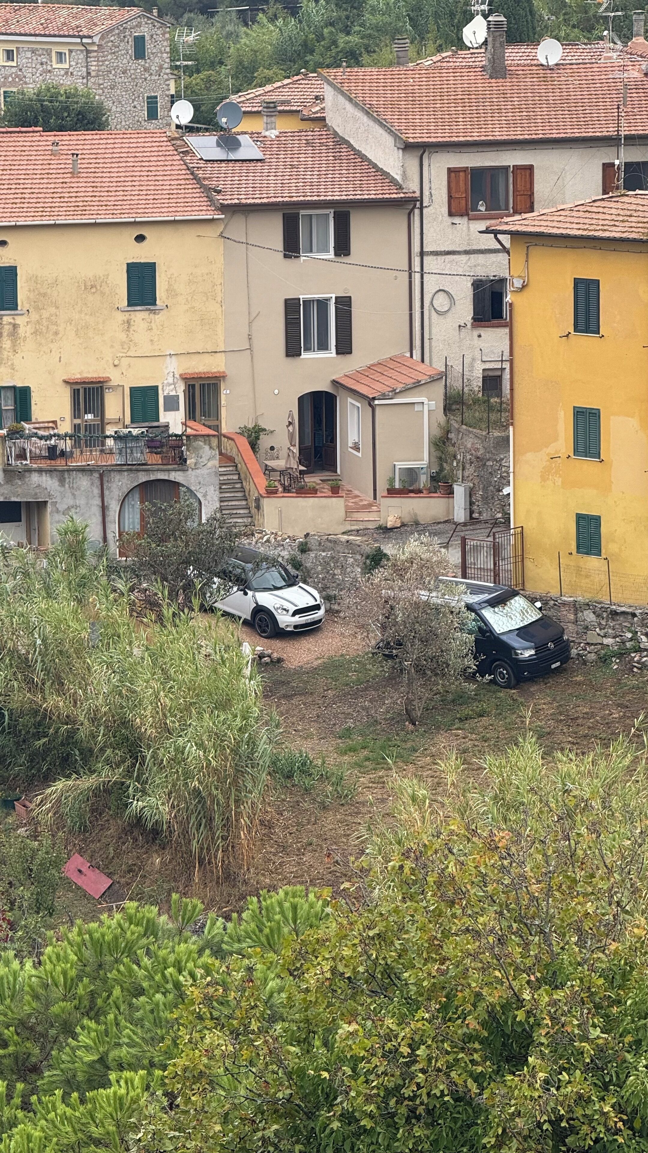 A residential area with terracotta-tiled roofs, stone buildings, and parked cars.