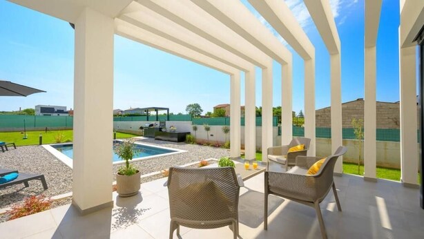 Un espacio al aire libre techado con asientos, una piscina y vistas a un campo deportivo.