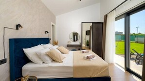 Un dormitorio moderno con una cama grande, una mesita de noche, un espejo y vistas a un área verde exterior.
