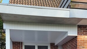 Ein modernes Haus mit überdachter Terrasse, großen Glasfenstern und einer Ziegelaußenwand.
