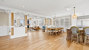 A spacious living area with a wooden floor, a dining table with chairs, and a kitchen area with a refrigerator. - Summer House - Luxury 5BR w/ Heated Pool Near Beach (Ocean City)
