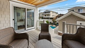 A covered balcony with wicker furniture, a sliding glass door, and a view of neighboring houses. - Summer House - Luxury 5BR w/ Heated Pool Near Beach (Ocean City)