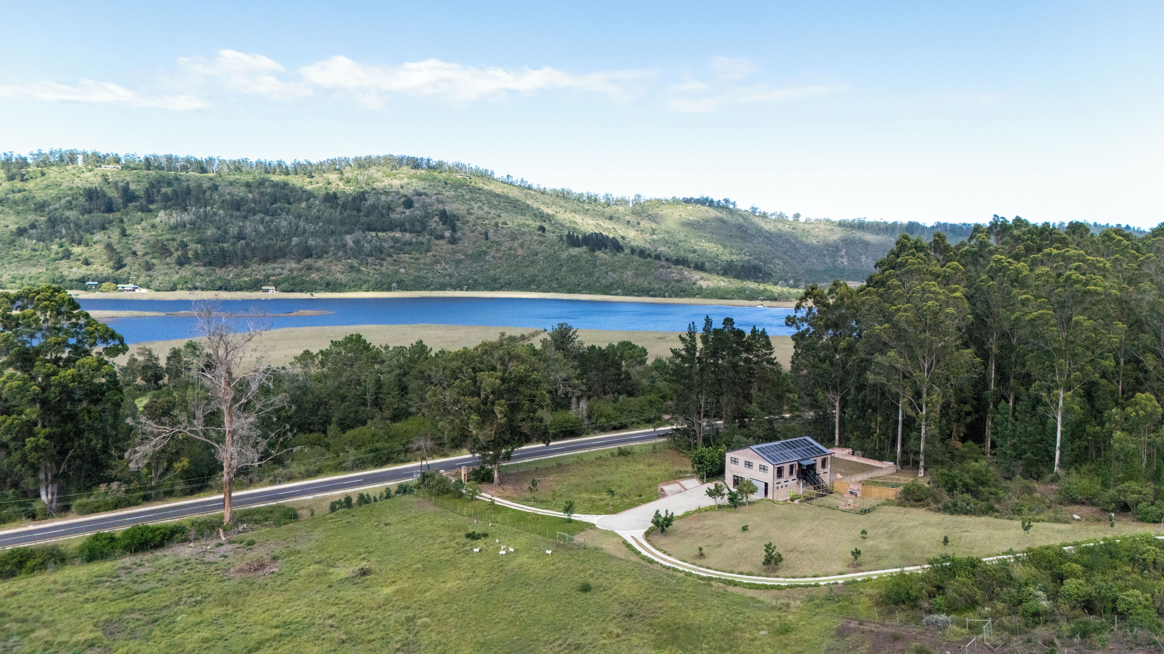 A rural landscape with a road, a small building with solar panels, and a lake.