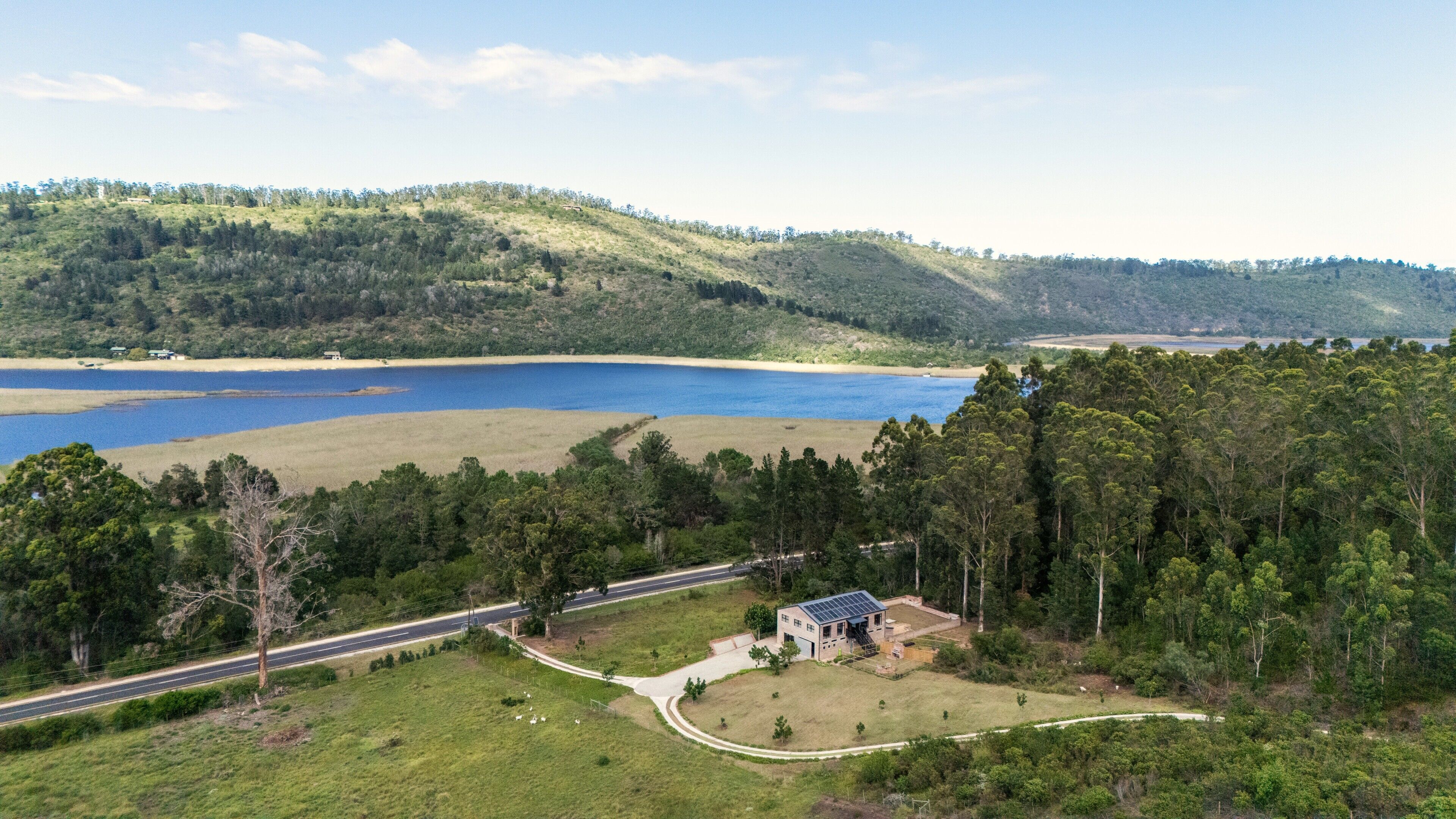 A rural landscape with a lake, a road, and a small building with solar panels.