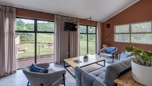 Et rummeligt værelse med stort vindue, fladskærms-tv, sofa, sofabord og en potteplante.