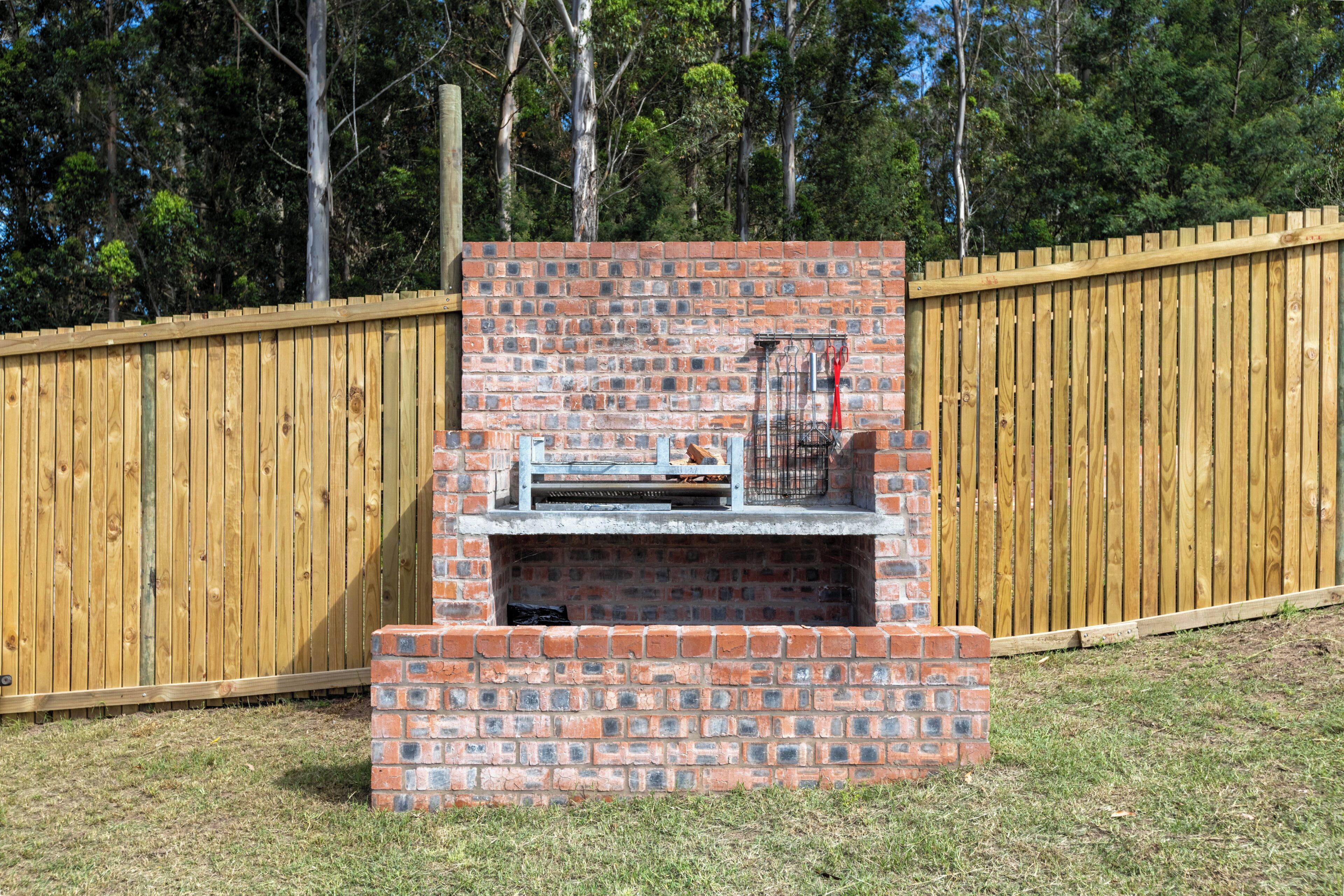 Een bakstenen barbecue met schoorsteen, omgeven door een houten hek en gazon.