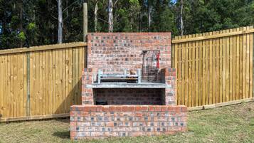 Een bakstenen barbecue met schoorsteen, omgeven door een houten hek en gazon.
