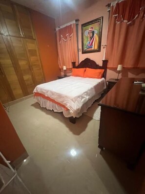 A bedroom with a bed, a wardrobe, a desk, and a painting on the wall. - Bello Apartamento en Santiago con Todas las Comodidades (Santiago de los Caballeros)