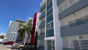 A modern building with a red vertical feature, multiple floors, and a parking area with cars. - Bello Apartamento en Santiago con Todas las Comodidades (Santiago de los Caballeros)