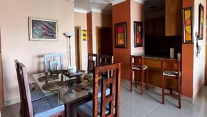 A dining area with a glass table, wooden chairs, a ceiling fan, and artwork on the walls. - Bello Apartamento en Santiago con Todas las Comodidades (Santiago de los Caballeros)